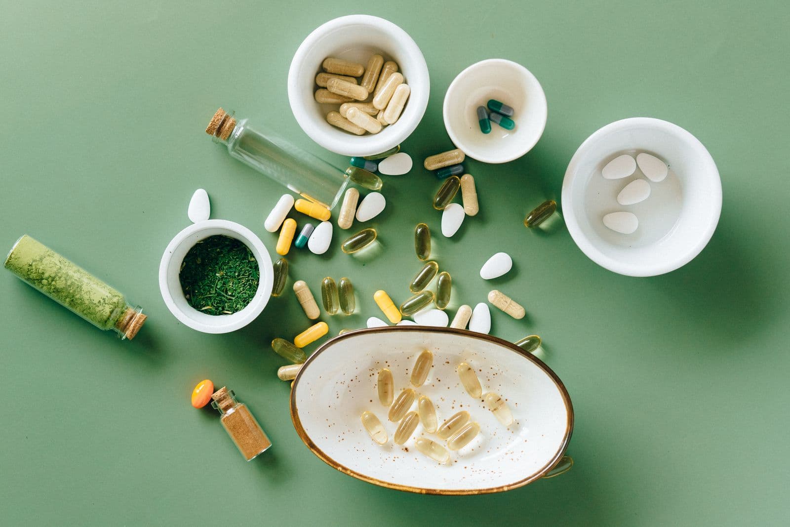 An assortment of PRIMA capsules and botanicals on a sage-green surface