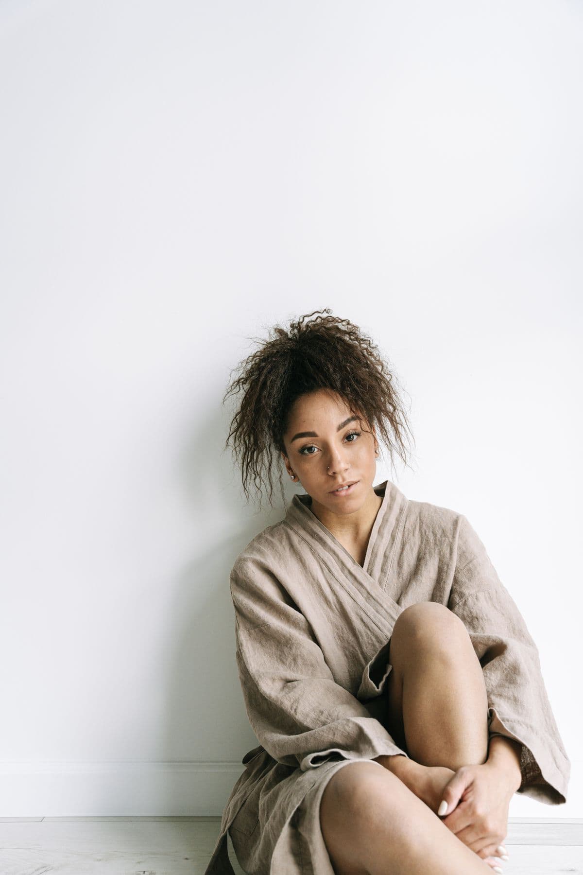 A woman sitting calmly against a white wall in a linen robe